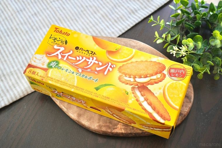 木のカッティングボードにのった黄色い箱のビスケットサンドとストライプの布とグリーン