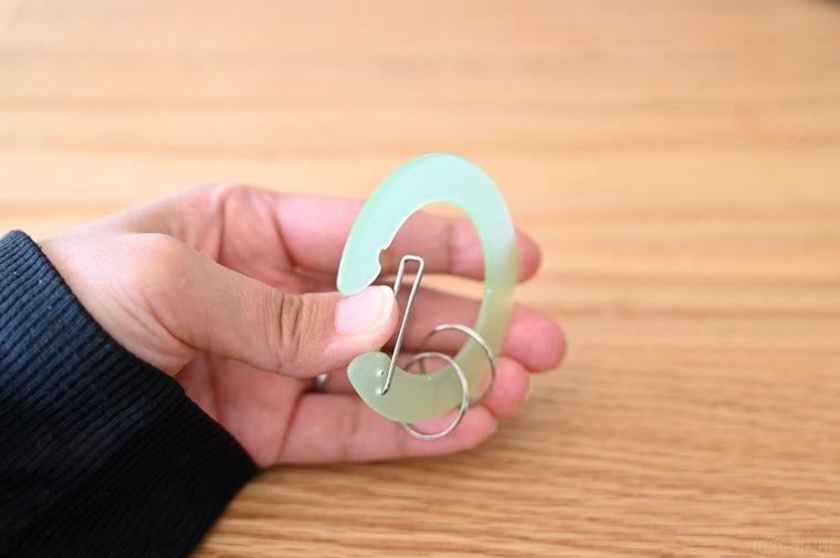 グリーンの丸型カラビナについている金属部分を親指で押している