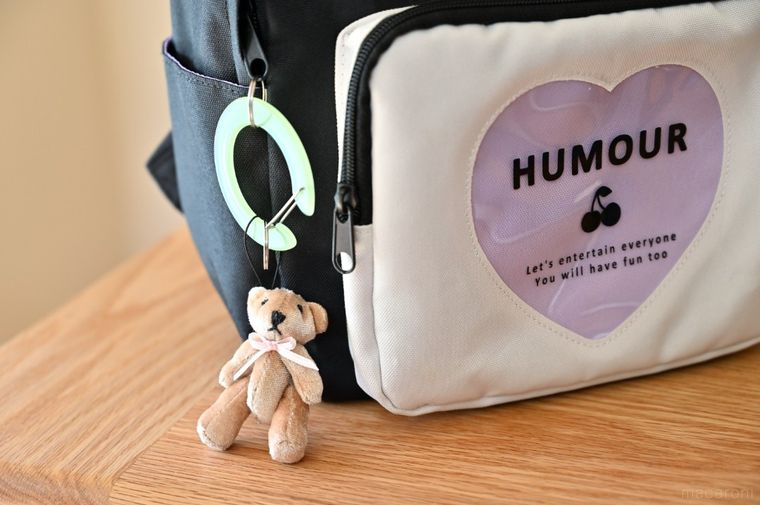 リュックにグリーンの丸型カラビナとくまのキーホルダーをつけている