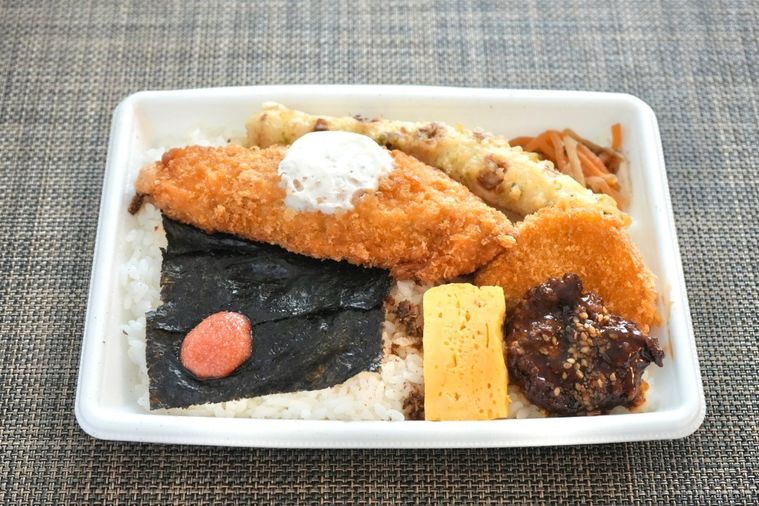 白い容器に盛られた白身魚のフライやちくわの磯辺揚げやコロッケがのったのり弁