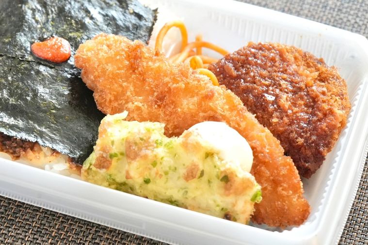 白い容器に盛られた白身魚のフライやちくわの磯辺揚げやコロッケがのったのり弁のおかずアップ