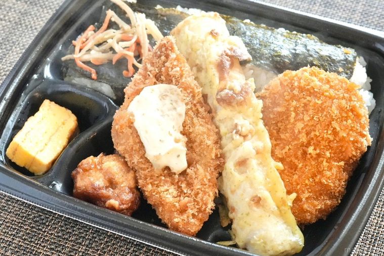 黒い容器に盛られた白身魚のフライやちくわの磯辺揚げやコロッケがのったのり弁のおかずのアップと湯気