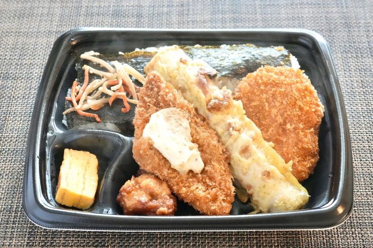 黒い容器に盛られた白身魚のフライやちくわの磯辺揚げやコロッケがのったのり弁