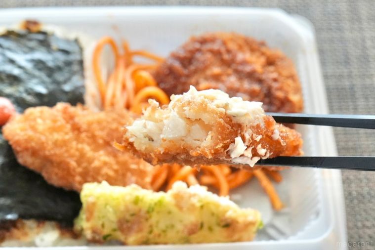 白い容器に盛られたのり弁の白身魚のフライの断面と黒い箸で持ち上げる様子