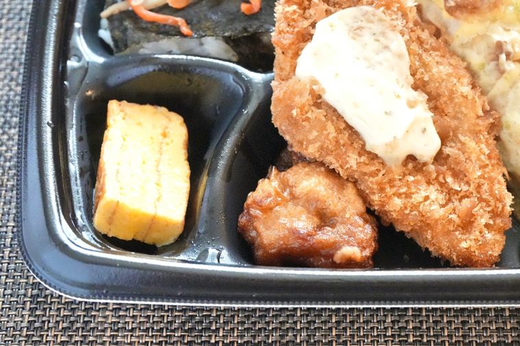 黒い容器に盛られたのり弁の白身魚のフライと唐揚げと卵焼き