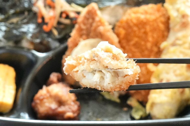 黒い容器に盛られたのり弁当のタルタルソースのせ白身魚を割って黒い箸で持ち上げる様子