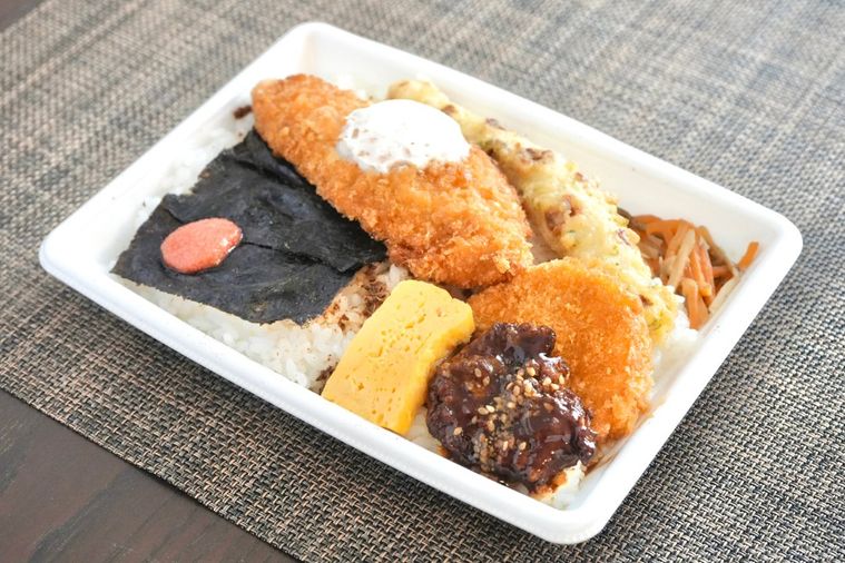 茶色いランチョンマットと白い容器に盛られた白身魚のフライのせのり弁当