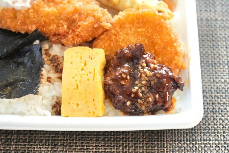 白い容器に盛られたのり弁の卵焼きとつくねとコロッケのアップ