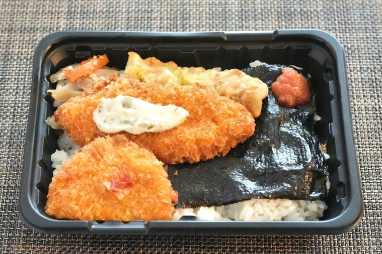 茶色いランチョンマットの上の白身魚のフライとちくわの磯辺揚げとハーフコロッケときんぴらごぼうのせのり弁当