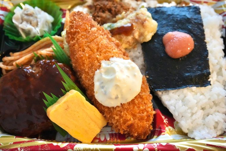 茶色いランチョンマットの上の白身魚のフライのせのり弁当とおかず