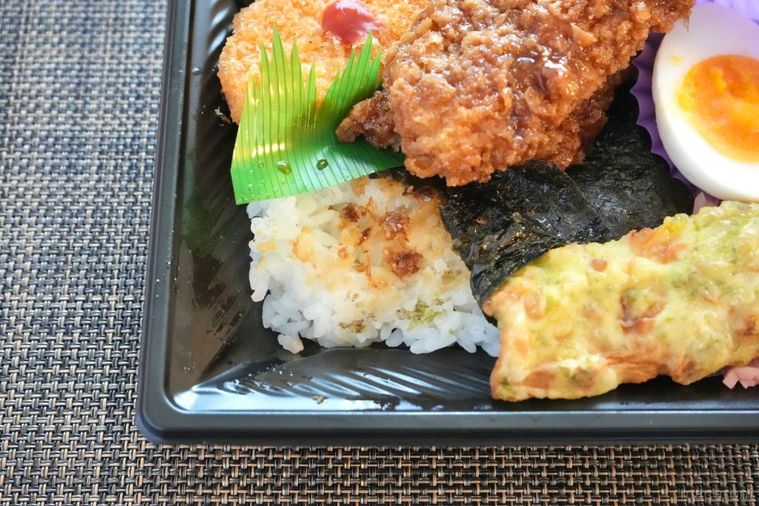 茶色いランチョンマットの上のイカフライのせのり弁当と味付きおかか