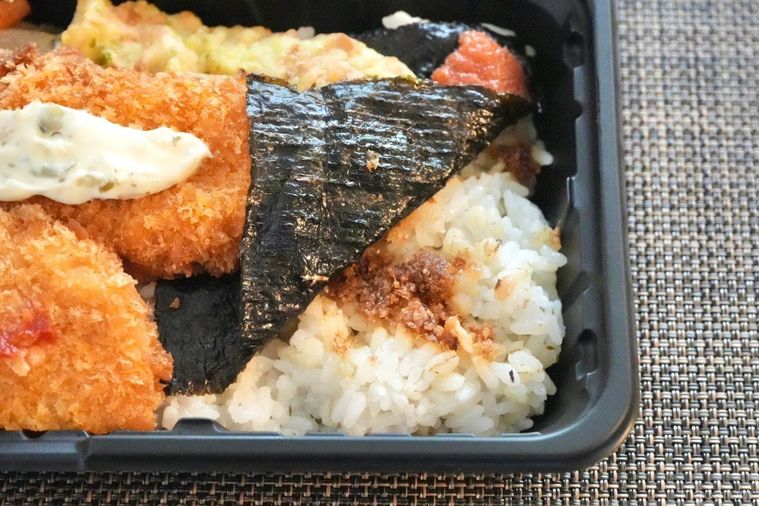 茶色いランチョンマットの上の白身魚のフライのせのり弁当と味付きおかか