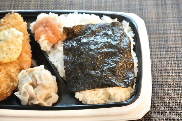 茶色いランチョンマットの上の白身魚のフライのせのり弁当とおかずと明太子