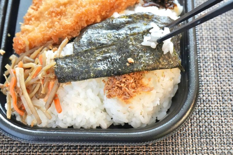 茶色いランチョンマットの上の白身魚のフライのせのり弁当の味付きおかかと昆布の佃煮