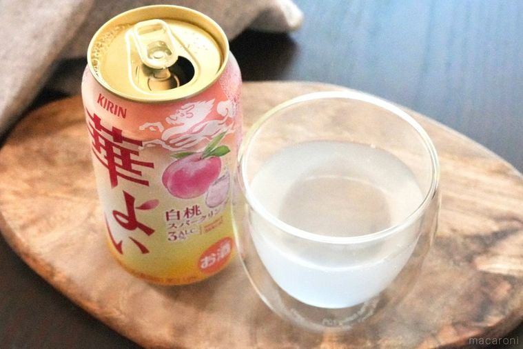 木のカッティングボードにのった白桃のピンク色の缶チューハイとグラスとグレーの布