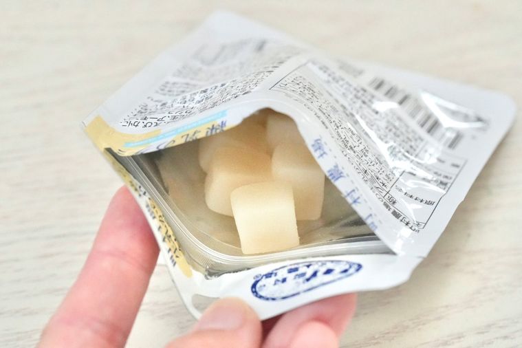 白い木目のテーブルと白色のパッケージの中のキューブ状の乳白色のグミ