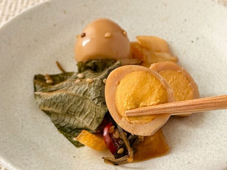 うずら卵とえごまの醤油漬の半分にカットされたうずら卵を箸で持っている様子