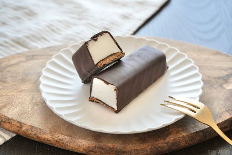 木のカッティングボードと白い皿にのったチョコレートコーティングのムースケーキの断面と金のフォーク