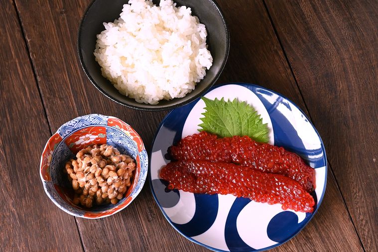 茶碗に盛られたごはんと小鉢に入った納豆、大葉とともに皿に盛り付けられたすじこが並んでいる