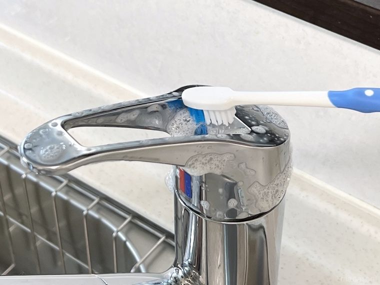 歯ブラシで蛇口の水垢をこすっている様子