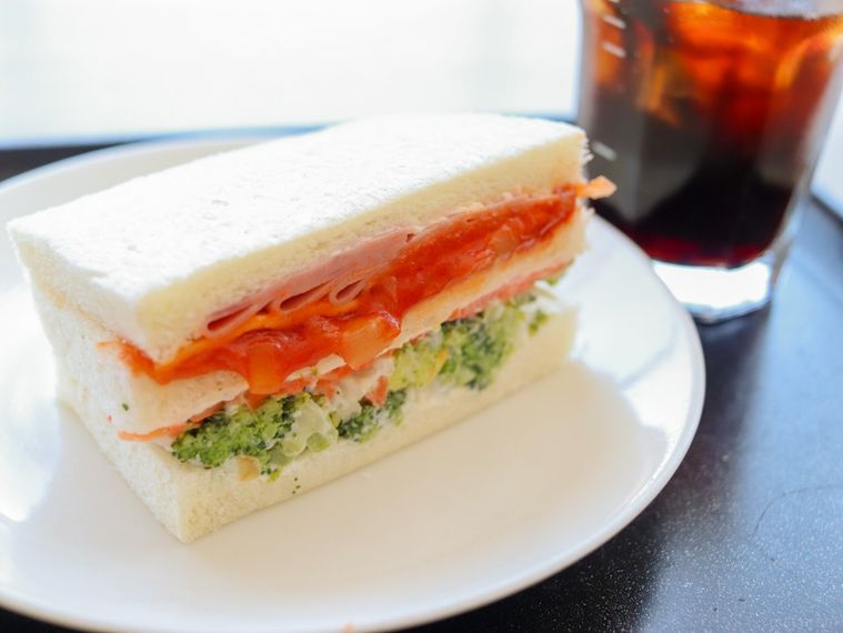 白いお皿にのったハムチーズサラダサンドとアイスコーヒーが黒いトレーの上に置かれている