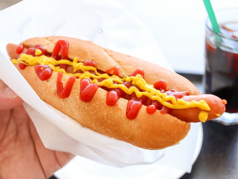 ケチャップとマスタードをかけたボールパークドッグ プレーンを手で持っている