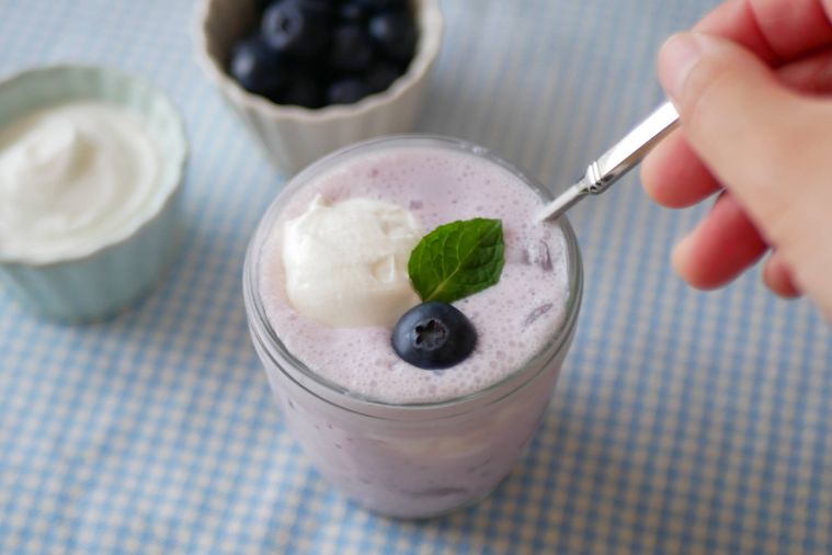グラスに入ったブルーベリーヨーグルトスムージーをスプーンでかき混ぜようとする様子