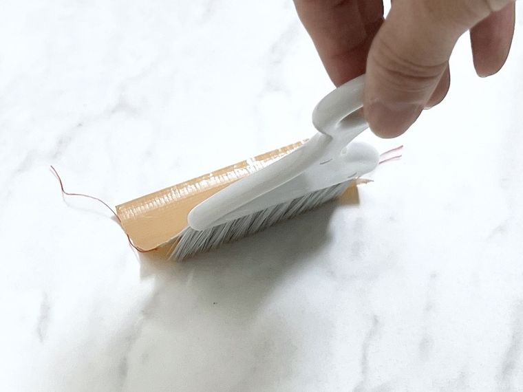 ガムテープを貼ったミニほうきで床を撫でている様子