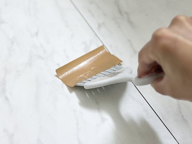 ガムテープを貼ったミニほうきで床を撫でている様子