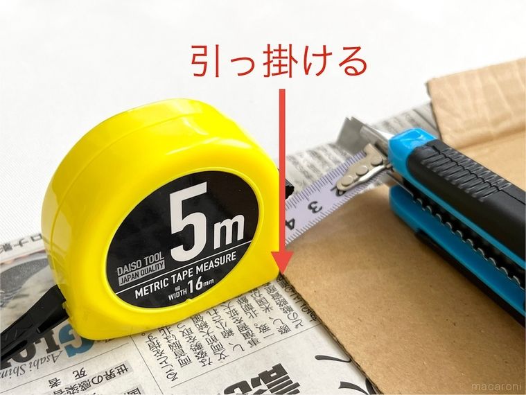 段ボールの端にメジャーの角を引っ掛けた様子