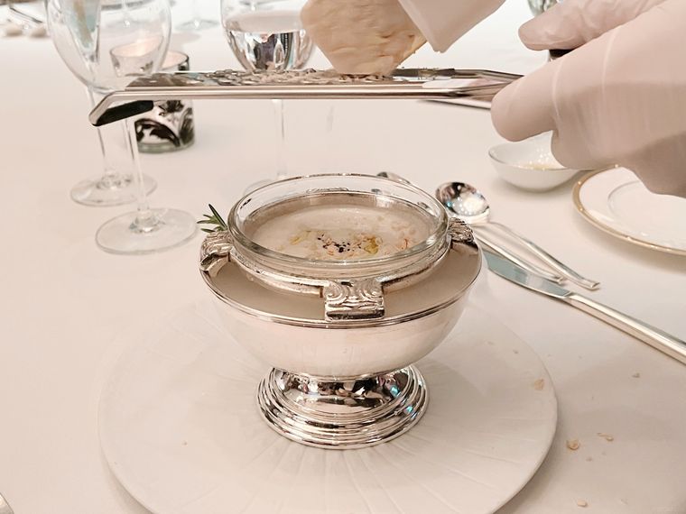 銀の器に入っているホワイトコーンの冷製スープにフォアグラテリーヌを削る様子