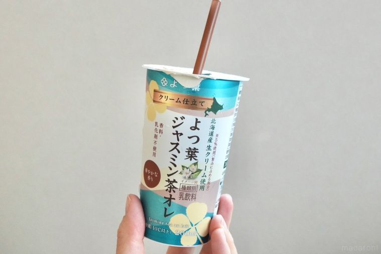 グレーの壁とジャスミン茶オレ入りのエメラルド色のカップを手に持つ様子