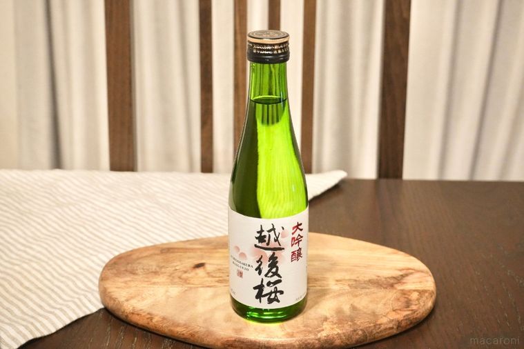 木のカッティングボードにのった日本酒の緑色の瓶とストライプの布