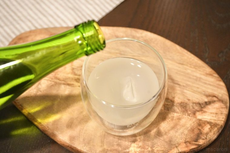 木のカッティングボードにのったカルピスと氷入りのグラスに緑色の瓶から日本酒を注ぐ様子