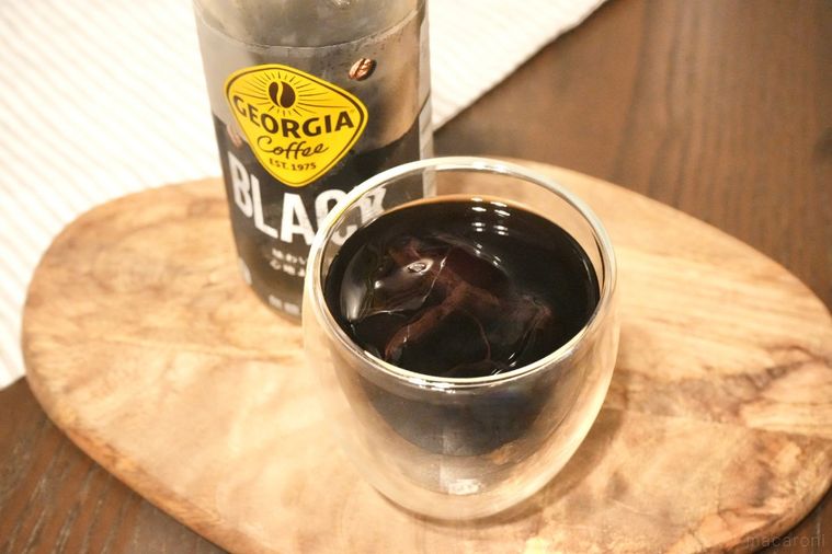 木のカッティングボードにのった氷入りのグラスにアイスブラックコーヒーを注いだ様子とペットボトル