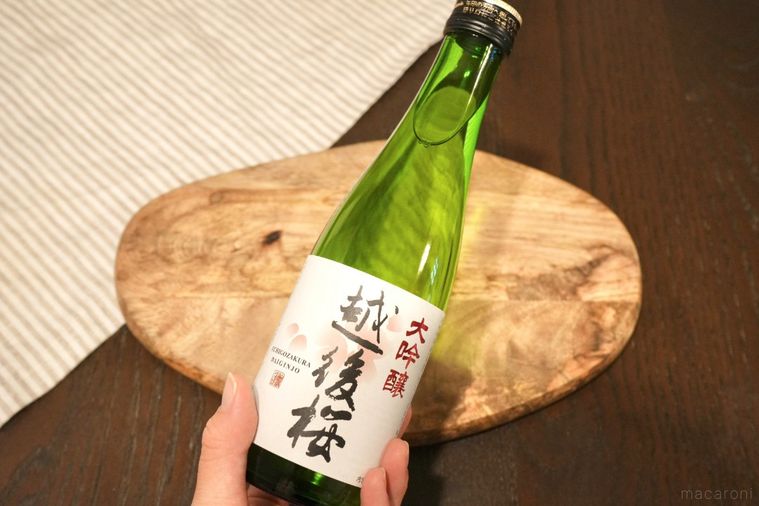 木のカッティングボードと緑色の日本酒の瓶を手に持つ様子