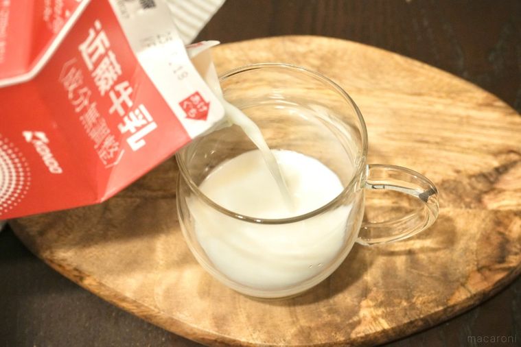 木のカッティングボードにのった日本酒入りのガラスマグに赤い牛乳パックから牛乳を注ぐ様子