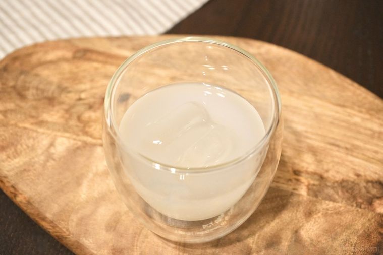 木のカッティングボードにのったカルピス原液と日本酒と氷入りのグラスとストライプの布