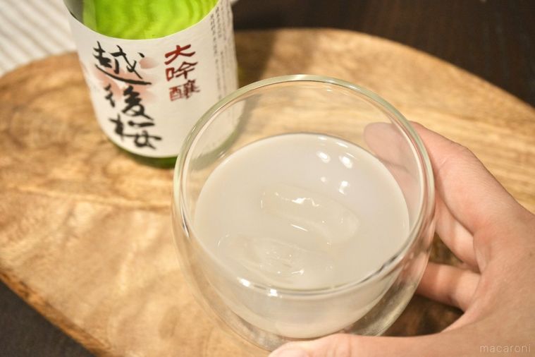 木のカッティングボードにのったカルピス原液と日本酒と氷入りのグラスと緑色の酒瓶とストライプの布