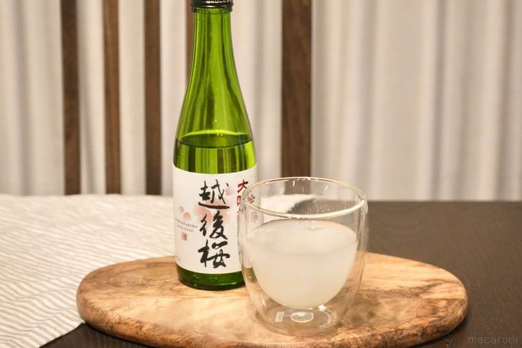 木のカッティングボードにのったカルピスと日本酒入りのグラスと緑色の酒瓶とストライプの布