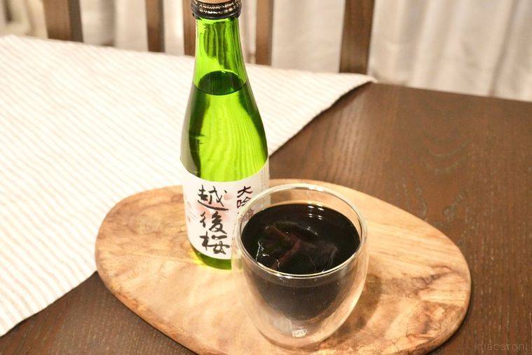 木のカッティングボードにのった日本酒の緑色の瓶と氷とアイスコーヒー入りのグラスとストライプの布