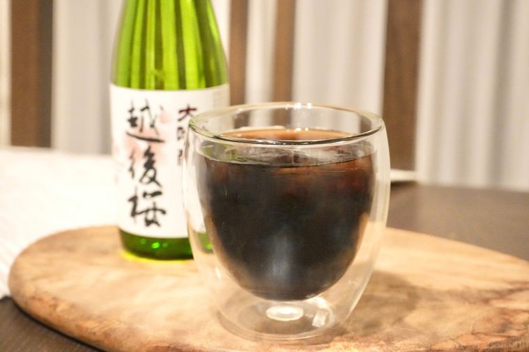 木のカッティングボードにのった日本酒の緑色の瓶と氷とアイスコーヒー入りのグラス