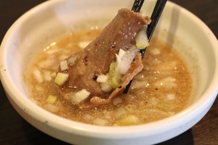 ねぎ塩だれに牛タンをつけている