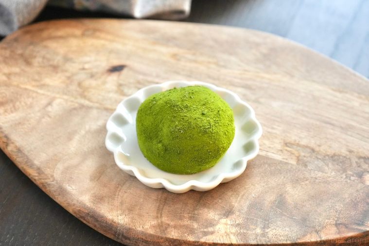 木のカッティングボードと白い小皿にのった緑色の抹茶大福とグレーの布