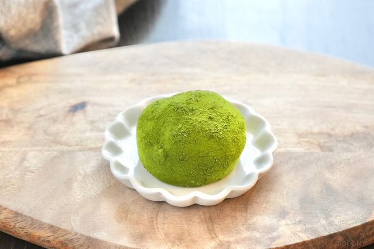 木のカッティングボードと白い小皿にのった緑色の抹茶大福とグレーの布