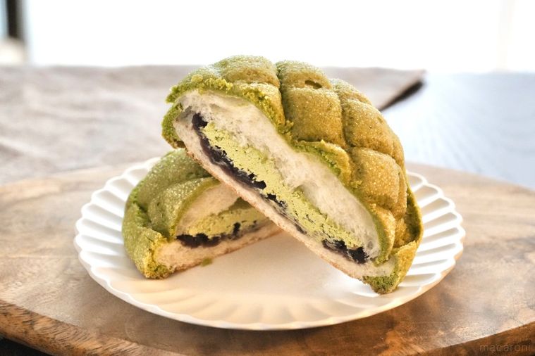 木のカッティングボードと白い皿にのった緑色の抹茶とあんこのメロンパンの断面とグレーの布