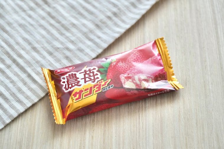 白い木目調のテーブルとストライプの布と苺味のブラックサンダー
