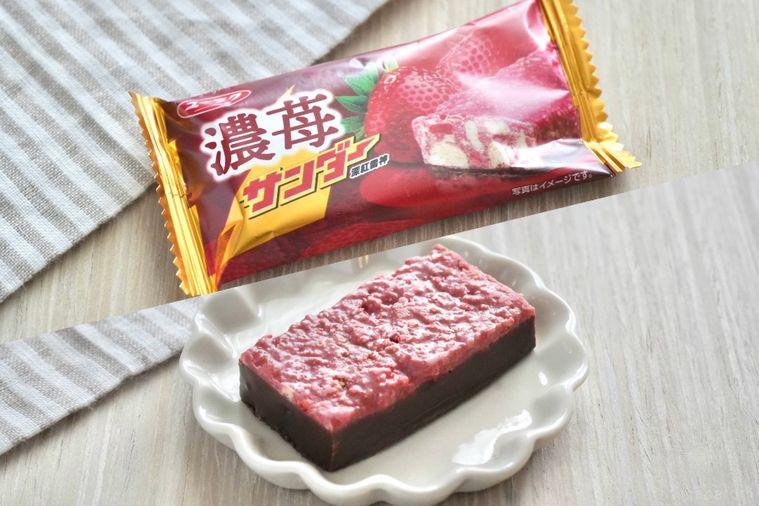 白い木目調のテーブルとストライプの布と苺味のブラックサンダーの赤いパッケージと白い小皿