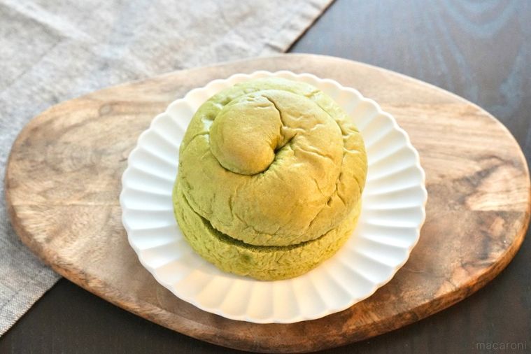 木のカッティングボードと白い皿にのった抹茶とミルクホイップクリームサンドの菓子パンとグレーの布