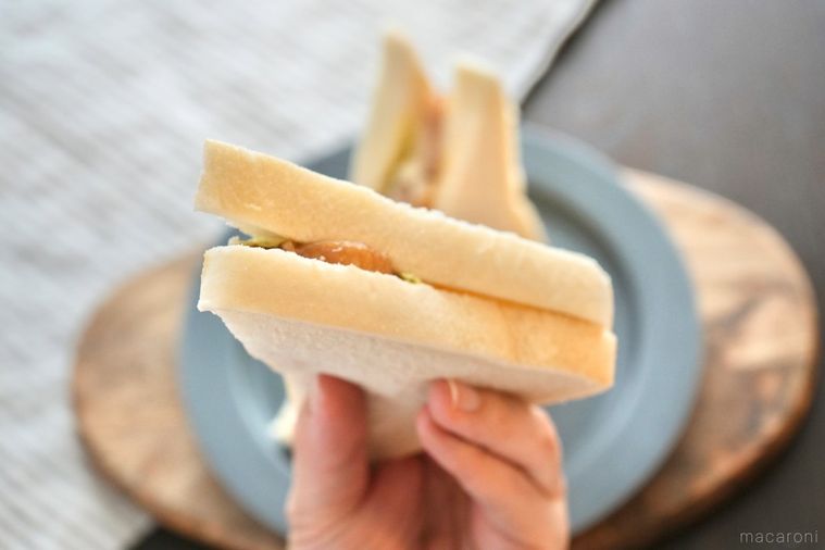 木のカッティングボードとグレーの皿にのった照り焼きチキン入りのサンドイッチを手に持つ様子とストライプの布